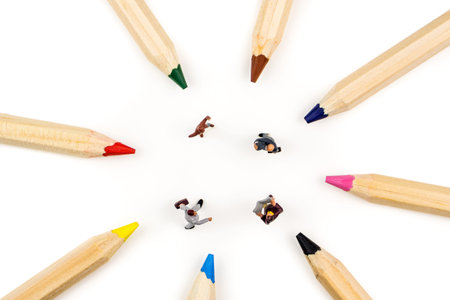 closeup of miniature figurines of businessmen having a meeting in a circle formed by multicolored pencils on white backgroundの写真素材