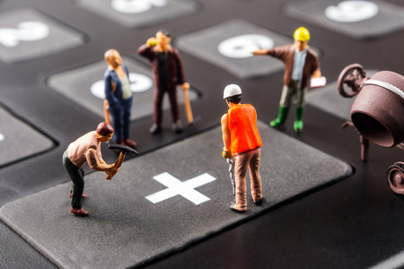 fixing the problem concept, closeup of miniature figurine of workers repairing plus sign on a big black calculatorの写真素材