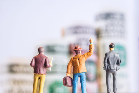 closeup of miniature figurines of businessmen standing in front of big defocused screen with american dollar banknotes forming an uprising graphの写真素材