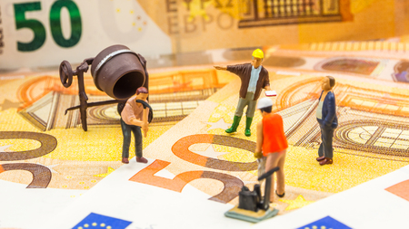 business concept, closeup of miniature figurine of workers repairing new 50 euro banknotesの写真素材