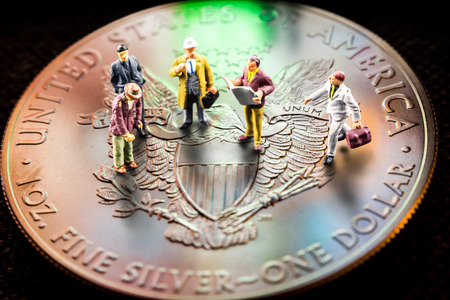 closeup of silver american eagle coin with a reflection of close digital device and miniature business men figurines having a meetingの写真素材