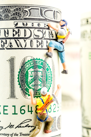 two miniature figurines climbing one hundred dollar banknoteの写真素材