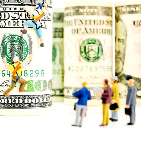 two miniature figurines climbing one hundred dollar banknote with businessmen audienceの写真素材