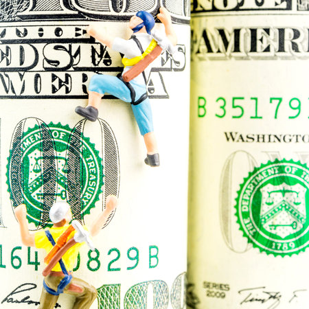 two miniature figurines climbing one hundred dollar banknote
