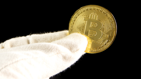 man with white gloves is holding a golden bitcoin in his hand on black backgroundの写真素材