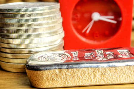 closeup of silver coins american one ounce eagles and brick laying on wooden background with red clock in the backの写真素材