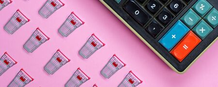 closeup of small miniature shopping carts taken from above with one big old calculator on pink backgroundの写真素材