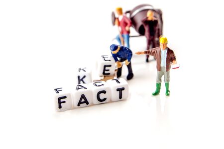fake and fact text formed of white dices with black letters and little miniature figurines of workers on white background, how can you distinguish between credible information and fake news, critical thinkingの写真素材