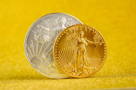 silver eagle and golden american eagle one ounce coins on golden backgroundの写真素材