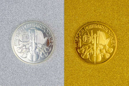 silver and golden austrian mint phillharmoniker one ounce coins laying on silver and golden background, image split in two halvesの写真素材