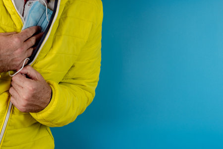 man in yellow jacket is using a protective mask against corona virus on blue background, high alert and the battle against the disease, COVID-19 SARS, SARS-CoV, virus 2020の写真素材