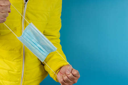 man in yellow jacket is using a protective mask against corona virus on blue background, high alert and the battle against the disease, COVID-19 SARS, SARS-CoV, virus 2020の写真素材