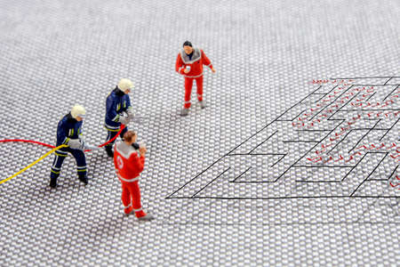 team of firefighters and doctors solving a difficult maze problem, finding best possible solution, five miniature figurines standing on complicated maze and thinking about the exit strategyの写真素材