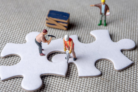solving problems fiting together of empty puzzle pieces, miniture figurines working on white puzzle...