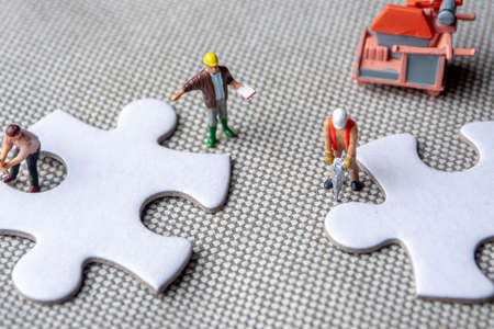 solving problems fiting together of empty puzzle pieces, miniture figurines working on white puzzle pieces, may be used in corporate topicsの写真素材