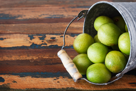 Brazilian fruit Spondias tuberosa (Brazil plum, imbu, umbu) in small bucket on wooden table. Selective focusの写真素材