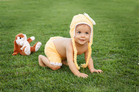 Cute happy smiling little baby girl in yellow clothing and funny hat with flower crawling in park on green grass. Selective focus. Toning effectの写真素材
