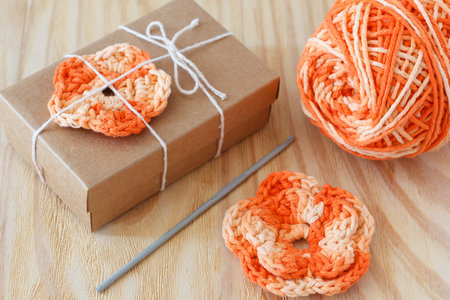Handmade orange crochet flowers decoration of gift with skein on wooden table. Selective focusの写真素材