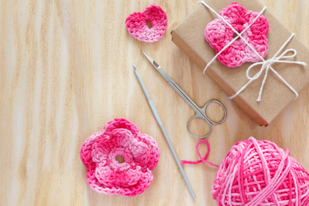 Handmade pink crochet flowers and heart for decoration of gift with skein and scissors on wooden table. Selective focusの写真素材