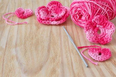 Handmade pink crochet flowers and heart with skein on wooden table. Selective focus. Copy spaceの写真素材