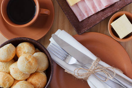 Brazilian snack pao de queijo (cheese bread) on brown plate with butter, cheese, ham, cup of coffee on wooden table. Selective focusの写真素材