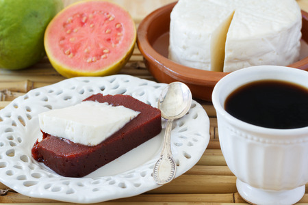 Brazilian dessert Romeo and Juliet on white plate, goiabada and Minas cheese with cup of coffee and fresh goiaba on wooden table bamboo. Selective focusの写真素材