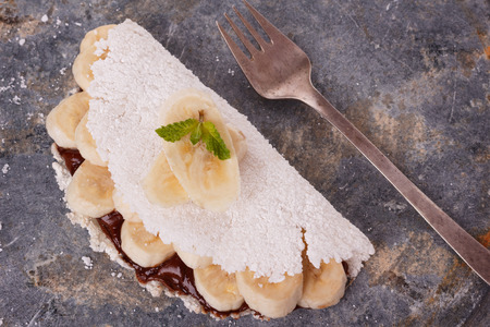 Casabe (bammy, beiju, bob, biju) - flatbread of cassava (tapioca) with banana and chocolate spread on gray stone background. Selective focusの写真素材