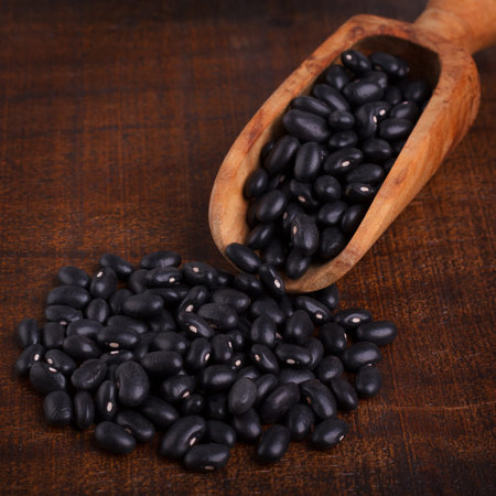 Black beans in scoop on wooden background. Selective focus. Copy space