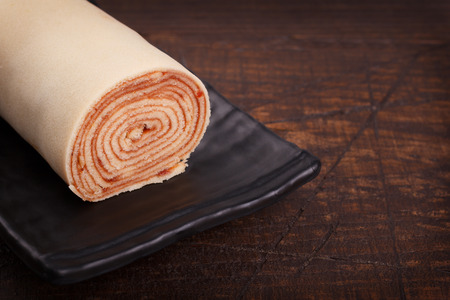 Swiss roll (cake) with red berry jam on wooden table. Selective focus. Copy spaceの写真素材