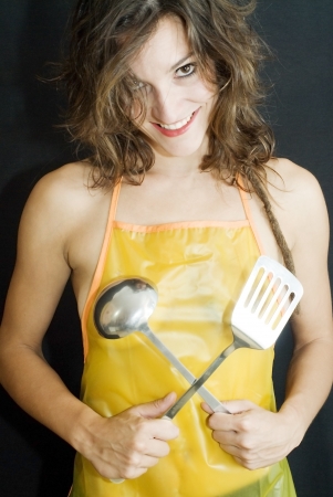 Pretty naked woman with apron, spatula and ladle over black backgroundの写真素材