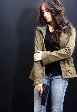 Beautiful Brunette Girl With Gun over black の写真素材