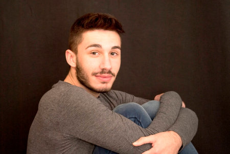 Handsome guy hugging himself  with beard on black backgroundの写真素材