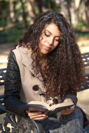 Beautiful woman on a park bench reading a book in autumnの写真素材