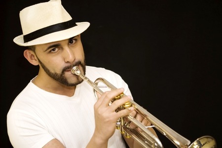 handsome guy playing a trumpet with beard and hat and  on black backgroundの写真素材