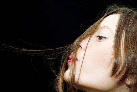 Portrait of Beautiful Young Woman Blowing Her Hair Over Black Backgroundの写真素材