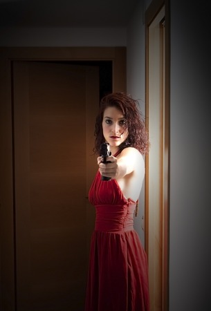 Portrait of Beautiful Young Woman  With a red dress and a gun in a hallwayの写真素材