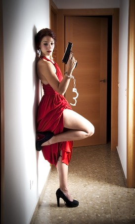 Portrait of Beautiful Young Woman  With a red dress, handcuffed and a gun in a hallwayの写真素材