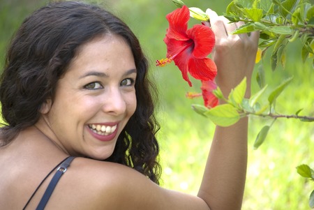Beautiful woman with red flower in a park on a sunny dayの写真素材