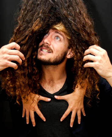 Handsome guy with the hair of a girl covering her face and he trying to pull her hair  on black background.の写真素材