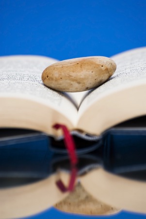 Book open with a single stone on it over a mirror with blue backgroundの写真素材