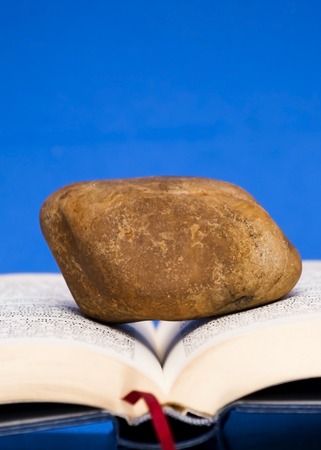 Book open with a single stone on it over a mirror with blue backgroundの写真素材