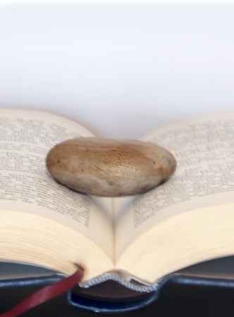 Book open with a single stone on it over a mirror with white backgroundの写真素材