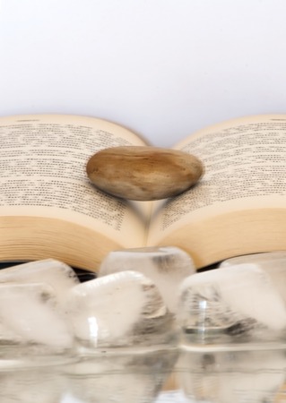 Book open with a single stone on it over a mirror with ice cubes with white backgroundの写真素材