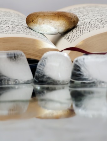 Book open with a single stone on it over a mirror with ice cubes with white backgroundの写真素材