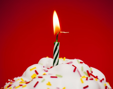 Cupcake with a lit candle over red backgroundの写真素材