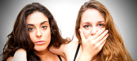 Portrait of two beautiful women, one covers her mouth to the other on a white background