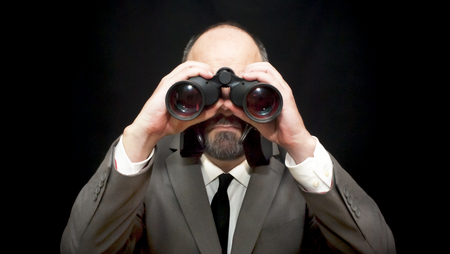 Handsome business man, bald and bearad, looking through binoculars over black backgroundの写真素材