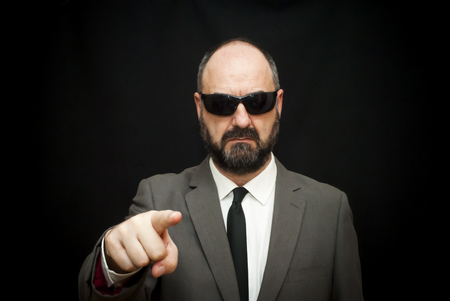 Handsome business man, bald and bearad, with sunglasses who is pointing forward with his index finger over black backgroundの写真素材
