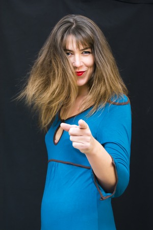 Portrait of a beautiful woman  in blue dress  pointing her fingers to the front on black backgroundの写真素材