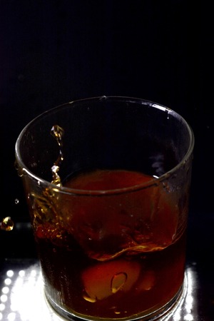 Glass of whiskey with falling ice cubesの写真素材